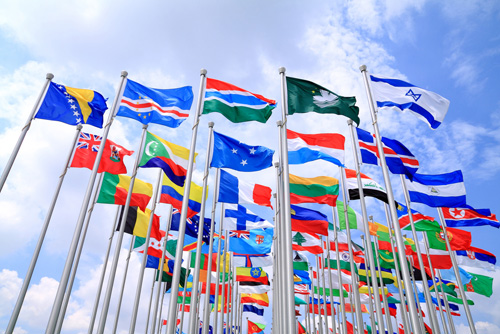 World flags on display, waving in the wind against blue sky and clouds.