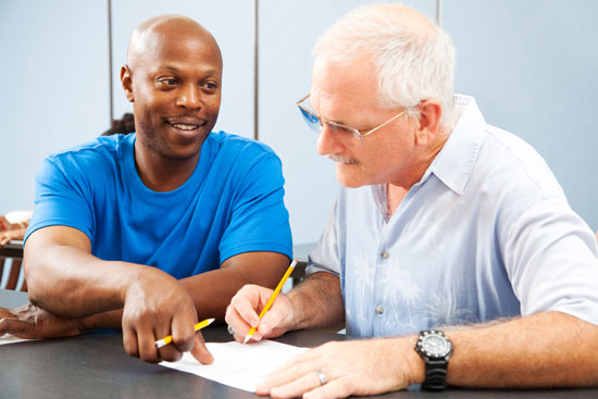 Two men, one older and one younger, work together at a desk.