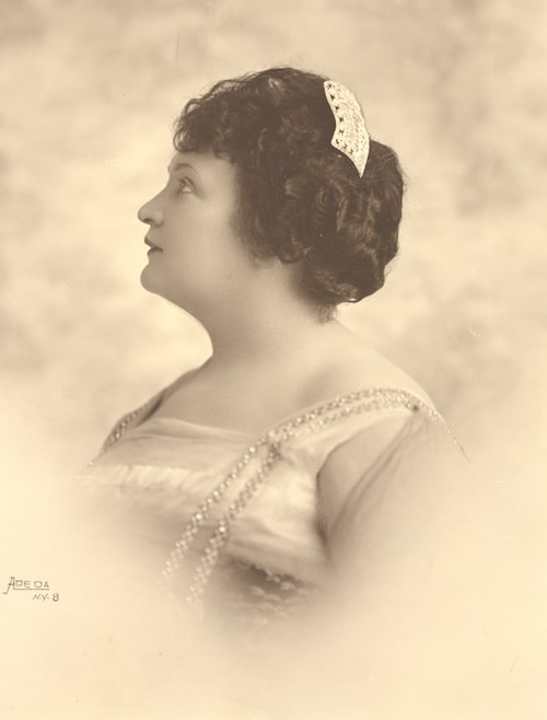 This head and shoulders photographic portrait of Anne in profile shows her looking quite glamorous. She wears what appears to be a large jeweled barrette in her hair. Her empire-style dress has a square neck and gathered bodice. Two long strands of sparkling beads are attached to the shoulder straps of the dress. Photo circa 1910.