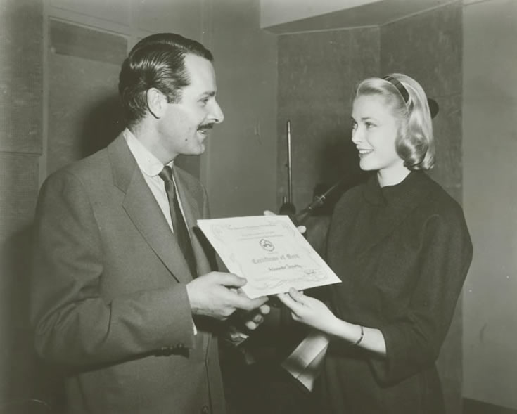 Narrator Alexander Scourby stands next to actor Grace Kelly in the recording studios of the American Foundation for the Blind. Kelly is presenting Scourby with the American Foundation for the Blind's Certificate of Merit for his work in recording books for the blind, March 4, 1956. Talking Book Archives, American Foundation for the Blind