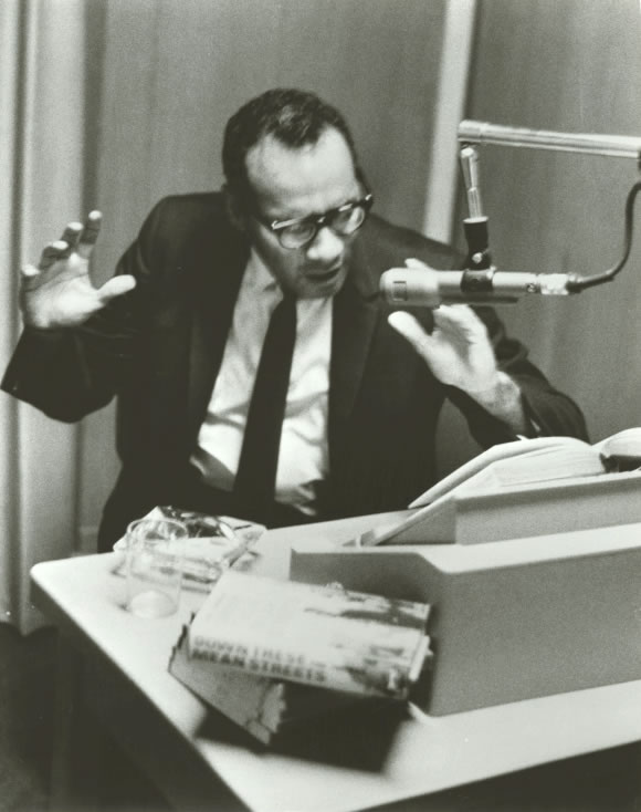 Author Piri Thomas recording his book Down These Mean Streets at the American Foundation for the Blind. He is seated behind a table. He faces a microphone and gestures with his hands as he reads from his book that lies open on the book stand in front of him, circa 1967. Talking Book Archives, American Foundation for the Blind.