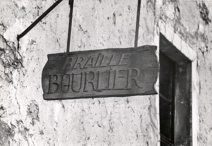 Close-up of the wooden sign on the side of Louis Braille's house. The sign reads "Braille Bourlier." Bourlier means harness maker. No date. 