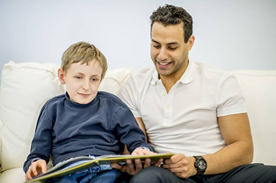 boy sitting on the couch with his father reading braille