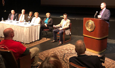 Audience members, panelists, and Isaac Lidsky listen to Lee Huffman who is standing at a lectern. 