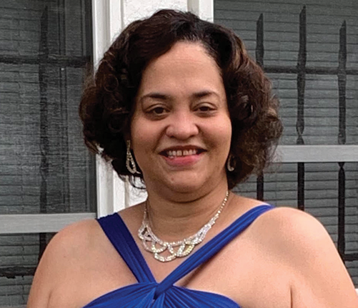 Stephanie Kaye Jones standing outdoor. She has chin-length hair and is wearing a blue dress and ornate necklace.