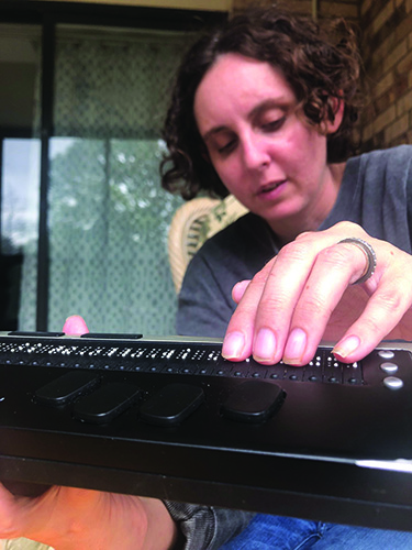 A fair skinned woman runs fingers along a braille display