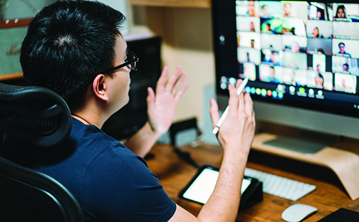 View over the shoulder of a person gesturing while talking, in front of a laptop computer with photos of various people on the screen