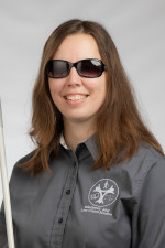 A smiling woman wearing dark glasses and holding a white cane.