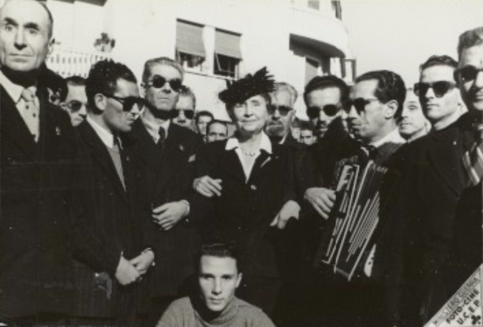 Three-quarter length image of Helen Keller surrounded by veterans during a visit to the Roman Institute for War Blind. 