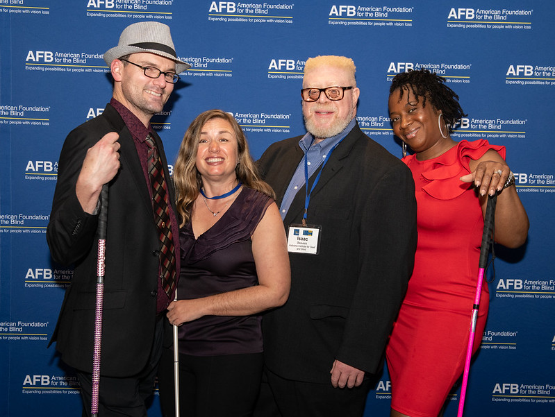 Four members of the Blind Leaders program smile as they pose in front of an AFB backdrop. 