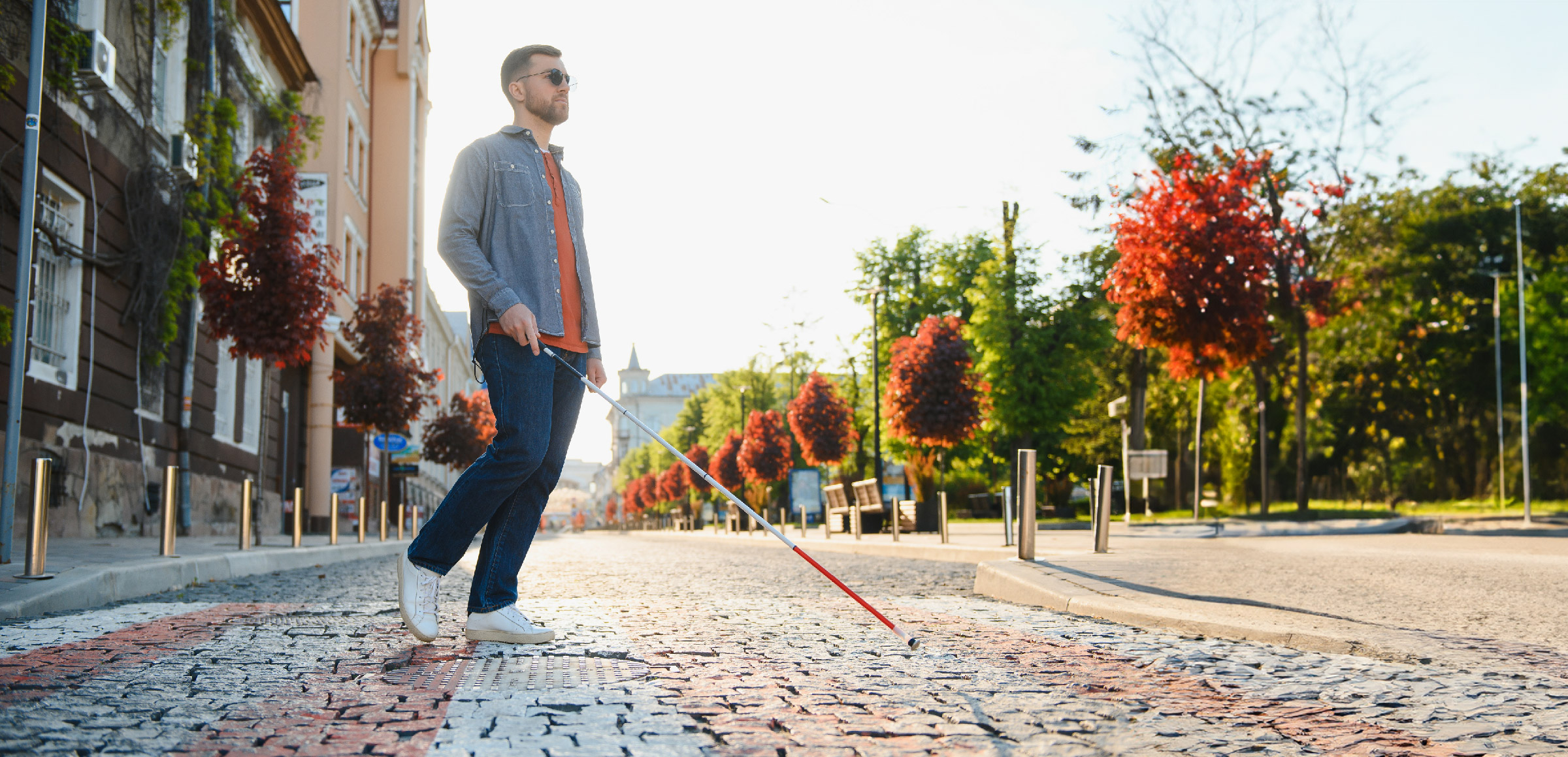 A person uses their white cane as they walk down a cobblestone street