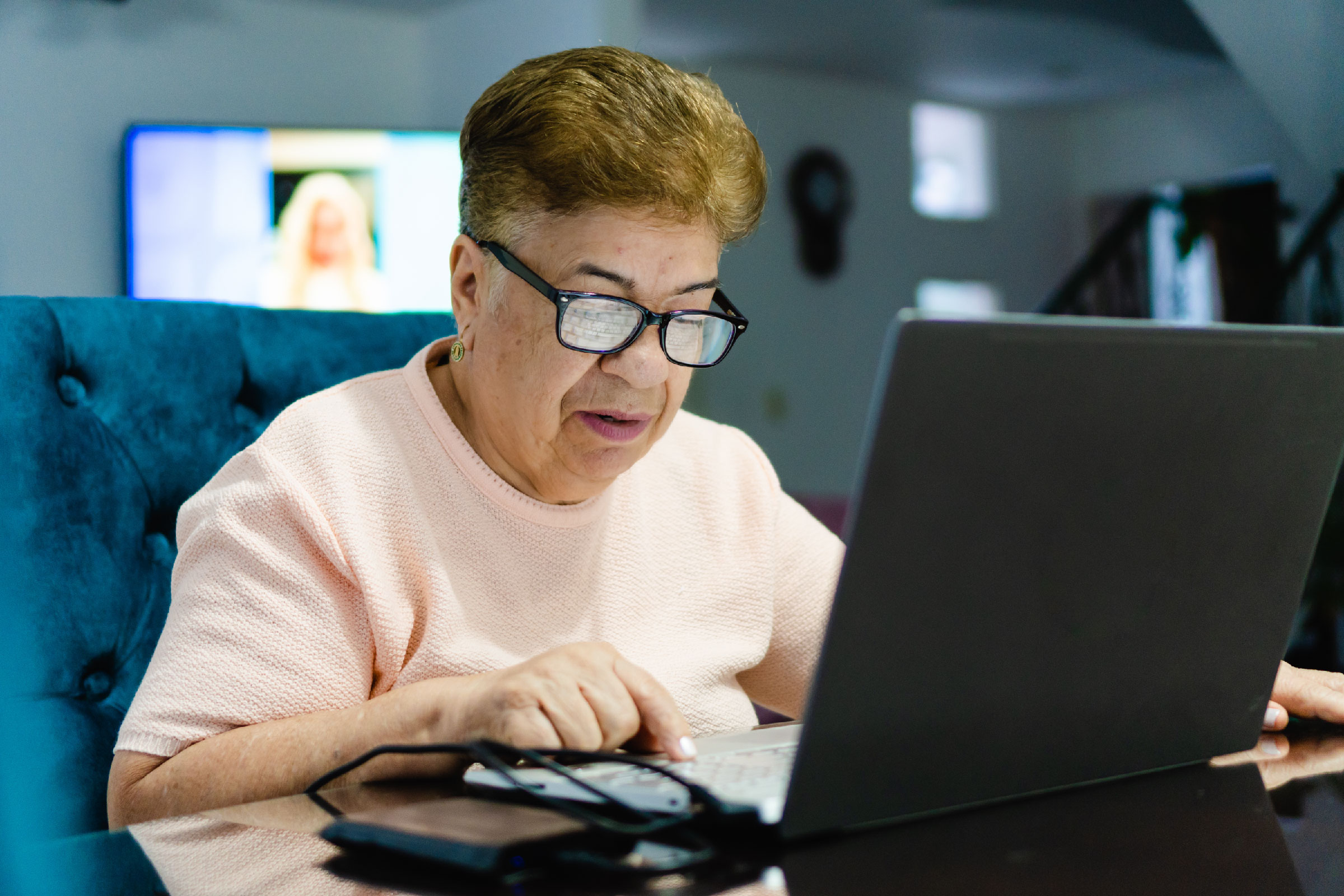 An older Latina woman wearing glasses uses a computer