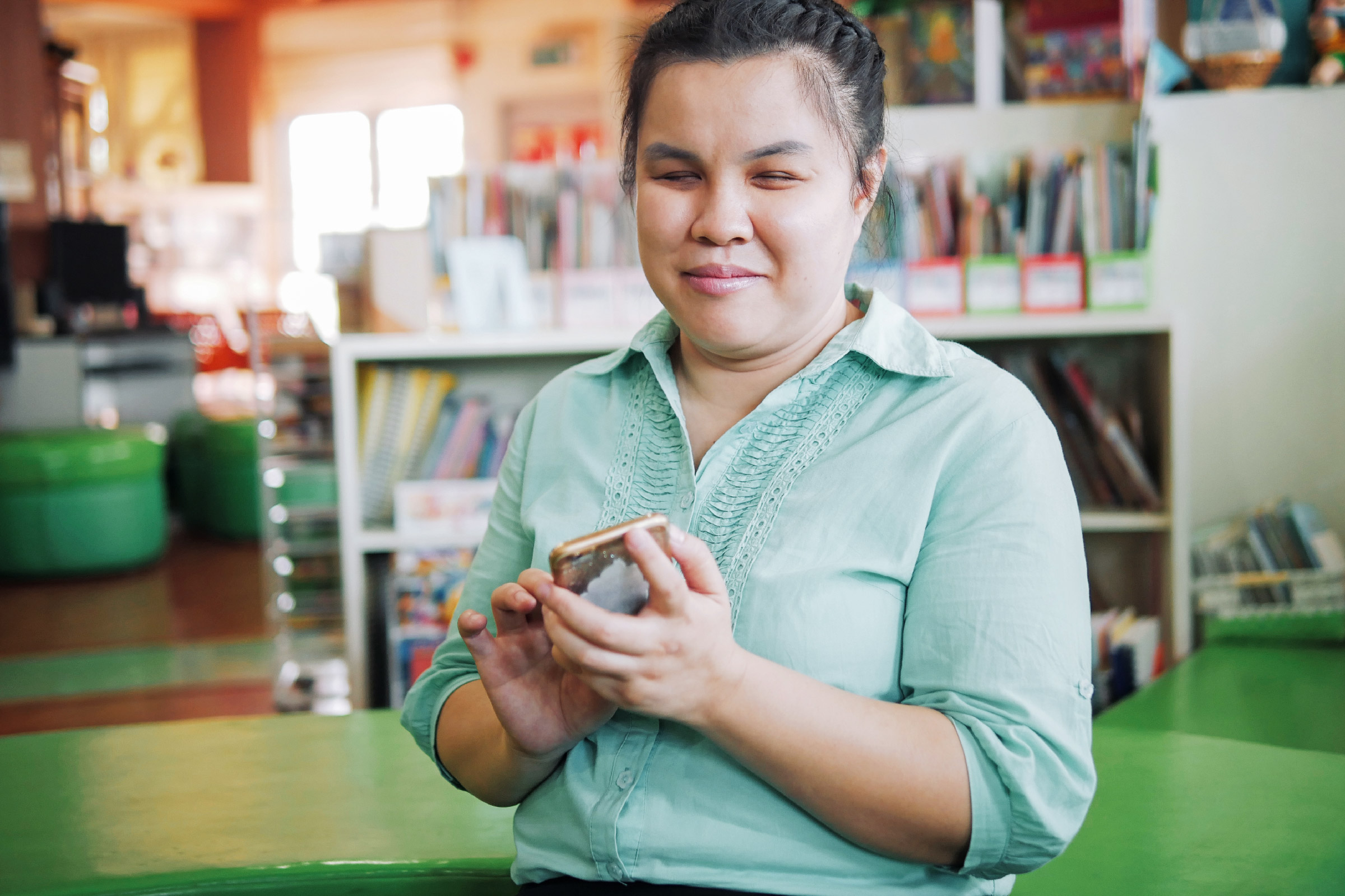 A young Asian blind person smiles as they swipe on their phone