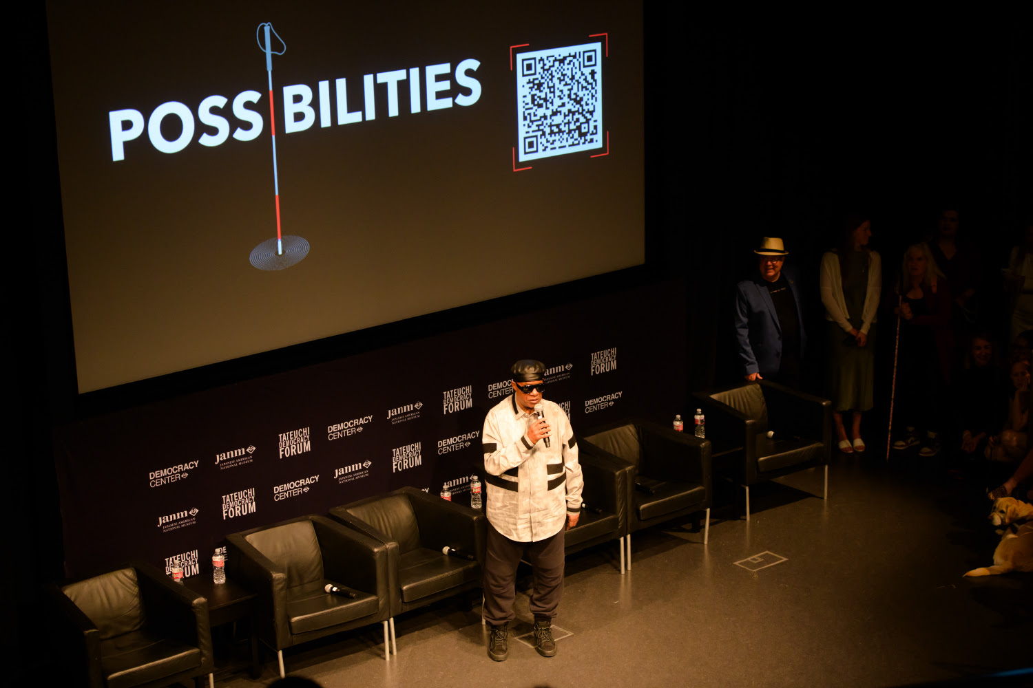 Stevie Wonder speaks in front of a screen with the Possibilities logo.