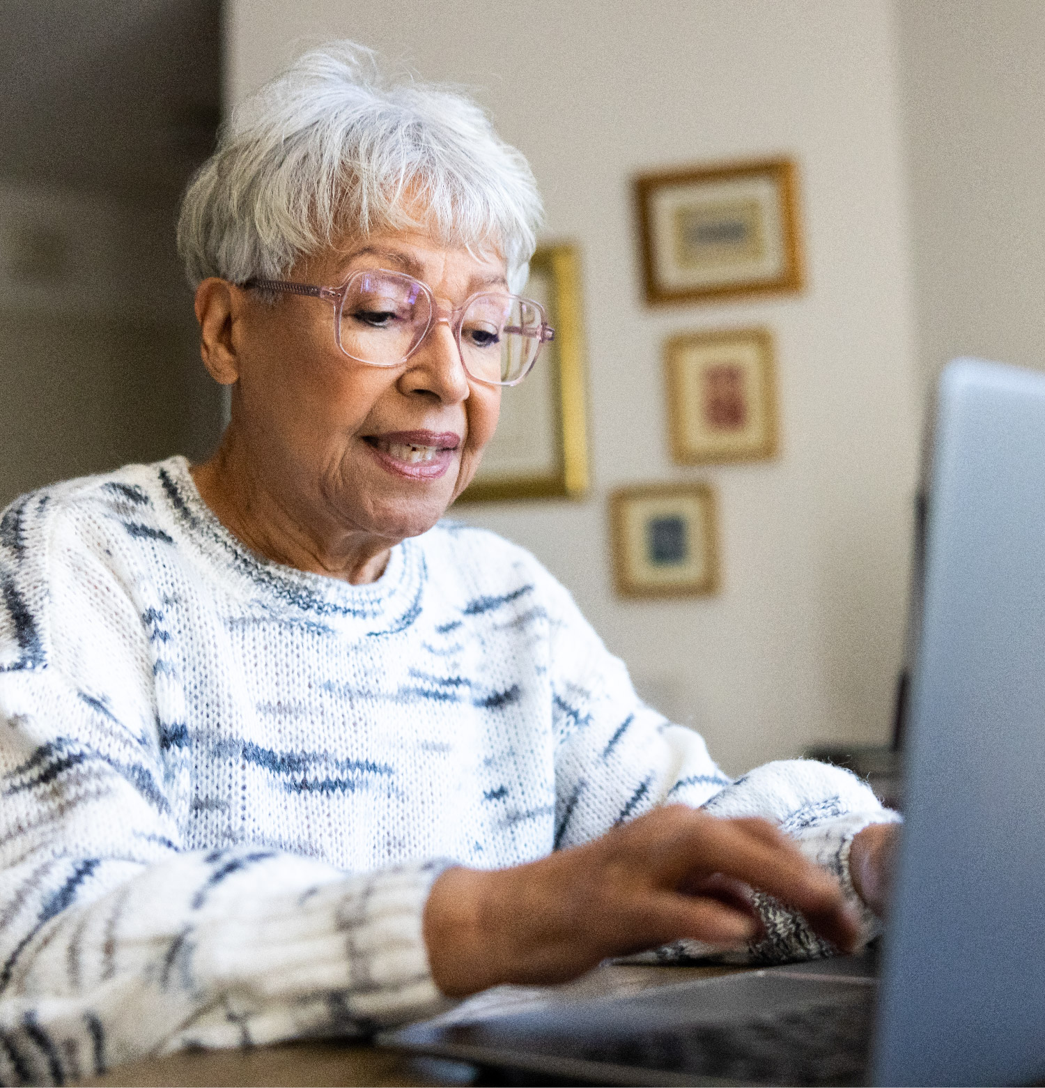 An older woman in her home typing on her laptop.