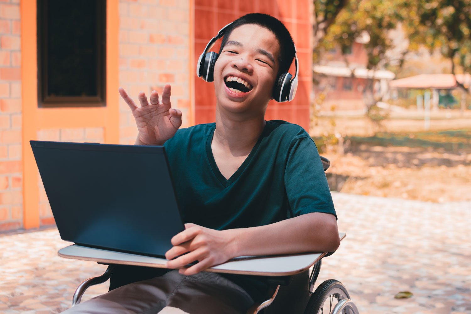 A young adult in a wheel chair using a tablet and listening through headphones.