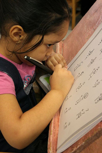 a serious young girl with low vision doing a large-print math worksheet with a black felt-tip pen