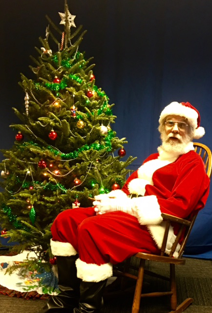 Ike Presley dressed as Santa, sitting by a decorated tree