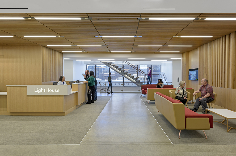 a wide shot of the Lighthouse entryway. It is a well-lit space filled with comfortable seating options, light wood paneling, and textural differences to mark the walkways.