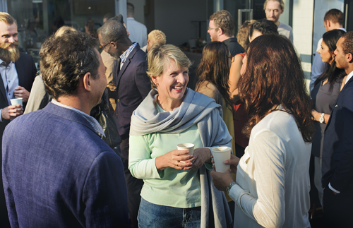 A group of committee members gather outside in the sun to converse and drink coffee.