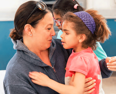 A teacher kneels to talk to a student. The student is reaching out to touch her teacher's shoulder.