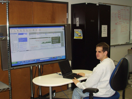 Randy Horwitz working on a laptop computer, with part of an IBM web page projected on a large screen.