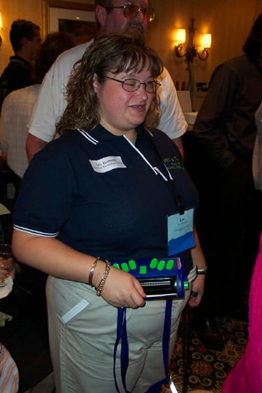 Exhibitor from Quantum Technology holds the Jot-a-Dot, a royal blue device with a bright green braille keyboard.