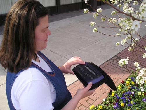 A woman holding the MPO 5500 and pressing one of the four-way rocker switches next to the refreshable braille display.