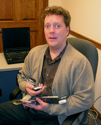 Photo of Darren Burton, looking bemused, with an armful of seven cell phones.