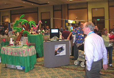 Photo of a crowded exhibit hall with some tropical-themed displays and a portable magnifier display in the foreground.