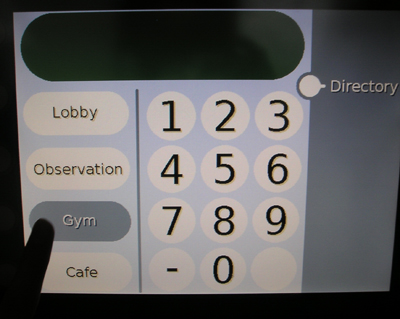 Photo of a touch screen with buttons along the left side labeled Lobby, Observation, Gym, and Cafe. A finger is touching the button labeled Gym, which is highlighted.