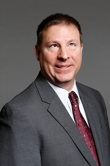 George Abbott, wearing a suit, against a gray background.