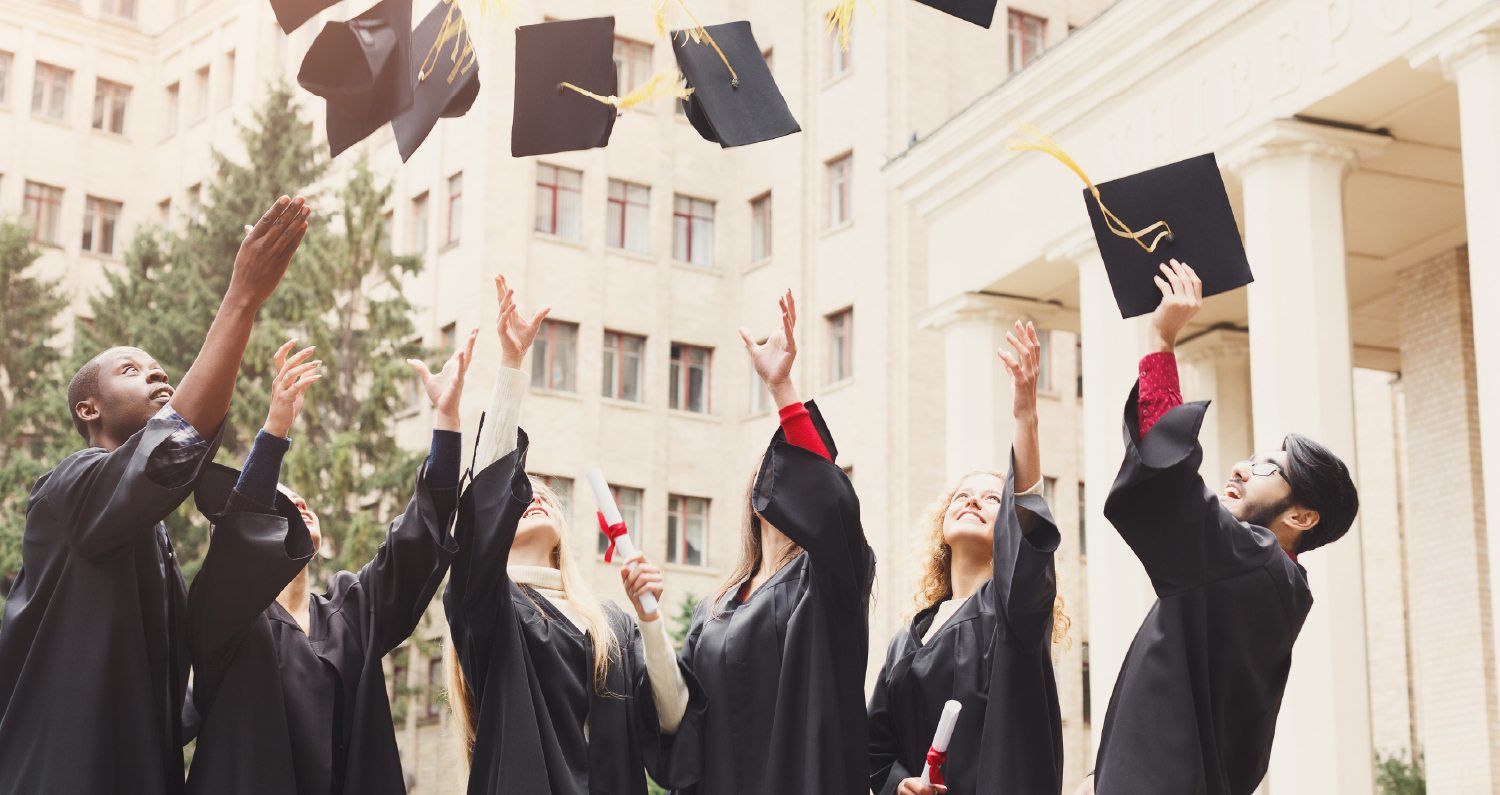 A group of students in graduation gowns throw their caps in the air.