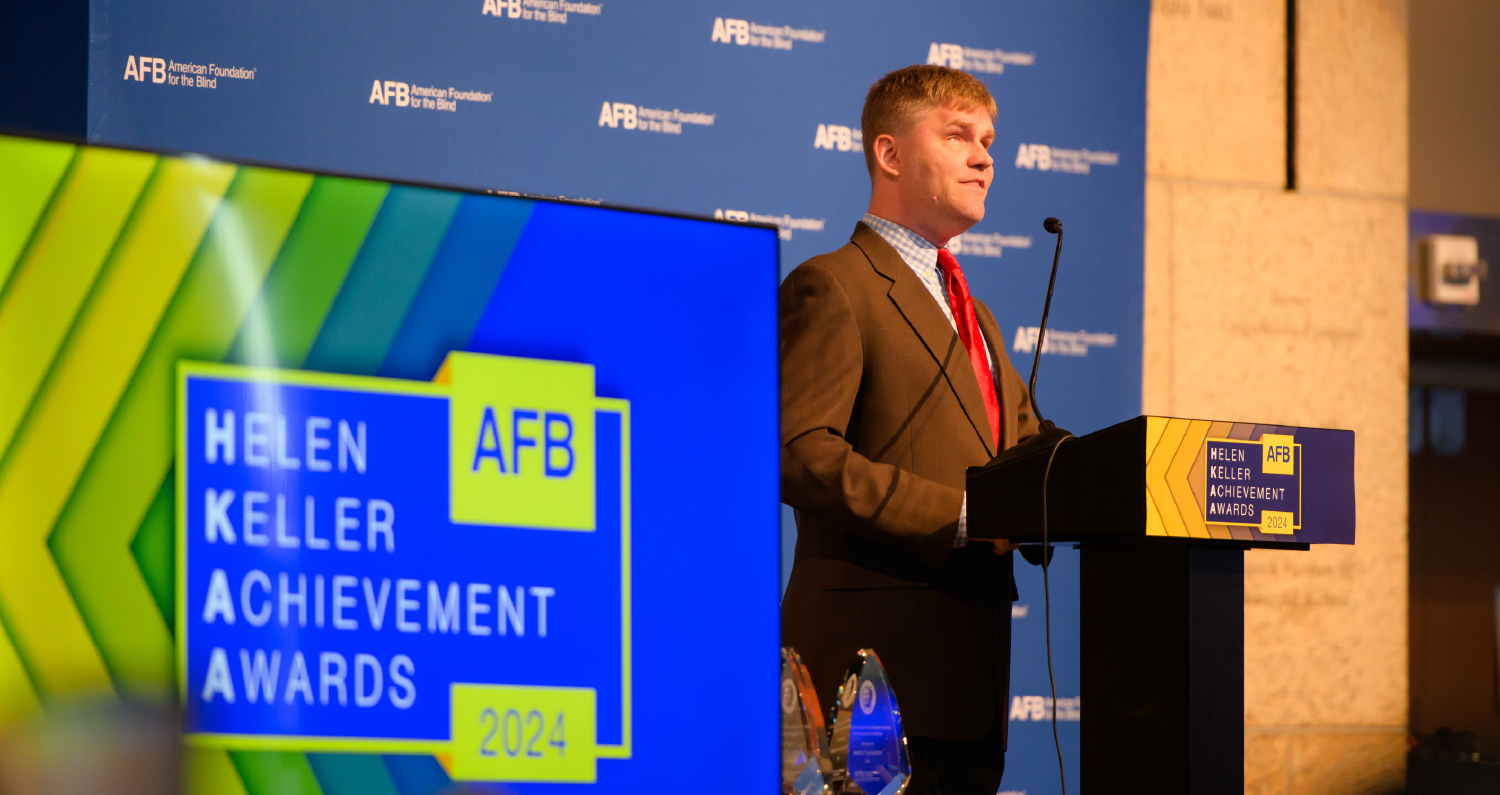 A man in a suit speaks on stage at an AFB event.